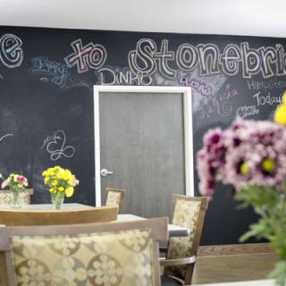A cozy room with a chalkboard wall adorned with welcoming messages, surrounded by tables and chairs with floral centerpieces.