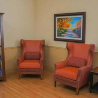 A cozy living room corner with two upholstered chairs, a colorful painting, and a bookshelf.