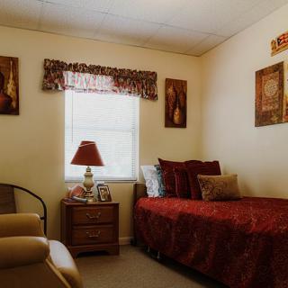 A cozy bedroom featuring a single bed with red bedding, a bedside lamp, and decorative wall art.