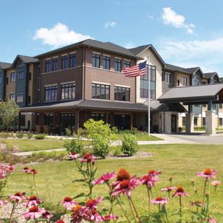 A modern multi-story building with a well-maintained garden featuring colorful flowers and an American flag flying in front.