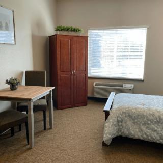 A cozy bedroom with a bed, table, chairs, and a wardrobe next to a bright window.