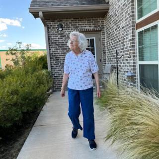 An elderly woman enjoying a stroll in her garden on a sunny day.