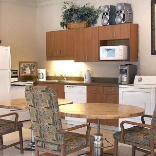 A modern kitchen with wooden cabinets, a table with chairs, and various appliances including a refrigerator and microwave.