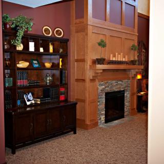 A cozy living room featuring a stone-faced fireplace and a dark wood bookshelf filled with books and decorative items.
