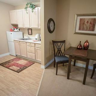 A cozy apartment kitchen and dining area featuring light wood cabinets, a small dining table with chairs, a refrigerator, and decorative elements.
