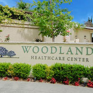A welcoming sign for the Woodland Healthcare Center, surrounded by lush greenery and flowers.
