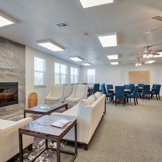 A spacious, modern living room with a fireplace and a conference seating area featuring blue chairs and neutral-toned sofas.