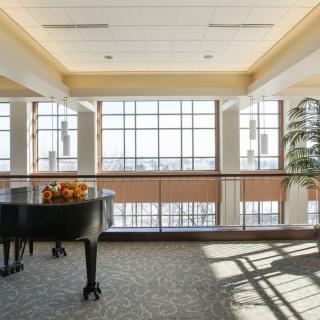 A grand piano sits in a sunlit room with large windows and a view.
