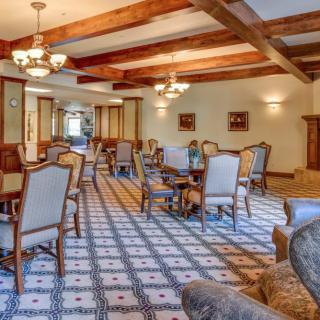 An elegant dining room with wooden beams, chairs, and tables arranged neatly under chandeliers.