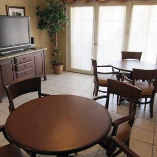A cozy dining area with round tables, chairs, and a TV by large windows.