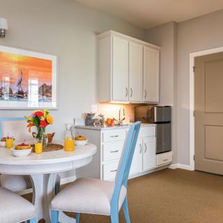 A cozy dining area with a round table and chairs, decorated in modern style with a kitchenette in the background.