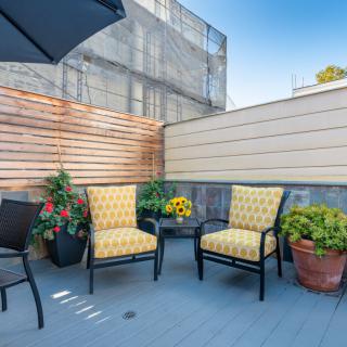 A cozy urban patio with stylish chairs and vibrant potted plants under a clear blue sky.