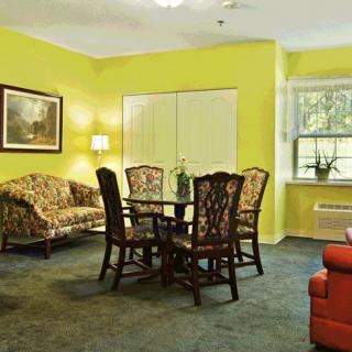 A cozy living room with a dining table, surrounded by chairs and a sofa, against bright yellow walls.
