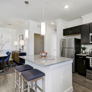A modern kitchen with an island countertop and stainless steel appliances, leading into a dining area.