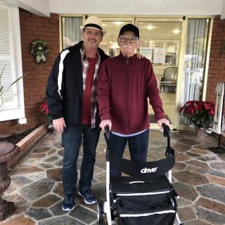 Two people standing outside a building, one using a walker.