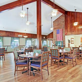 A spacious dining area with wooden flooring, tables, and chairs, featuring an American flag on the wall.