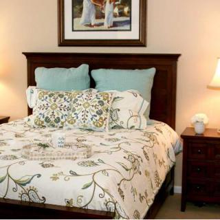 A cozy bedroom with a neatly made bed, featuring decorative pillows and a floral comforter, flanked by nightstands with lamps.