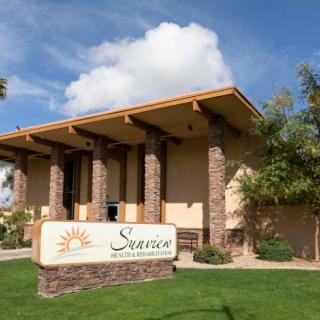 A modern building with a sign, surrounded by greenery and under a partly cloudy sky.