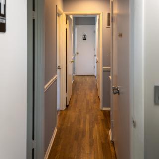 A narrow, well-lit indoor hallway with wooden flooring and multiple doors leading off the corridor.