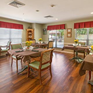 A cozy dining room with wooden floors, set with tables and chairs, and decorated with flowers.