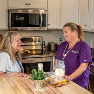 A friendly interaction between a caregiver and a senior in a kitchen setting, discussing food and healthy choices.