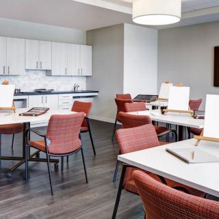 A modern meeting room with red chairs and tables, featuring a kitchenette in the background.