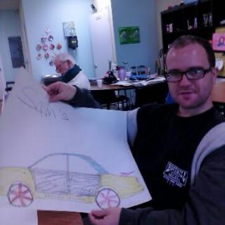 A person holding up a drawing of a car in an indoor setting.