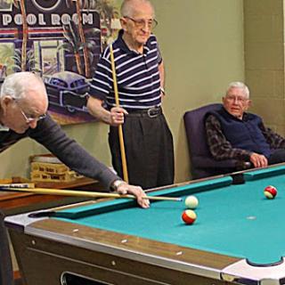 Three elderly men enjoying a game of pool together.