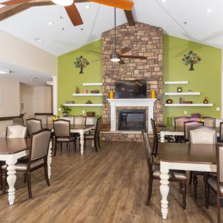 A cozy dining room featuring a stone fireplace, wooden tables and chairs, with decorative shelves and wall art.