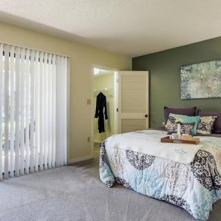 A cozy bedroom featuring a neatly made bed with decorative pillows, soft lighting, and a sliding glass door.