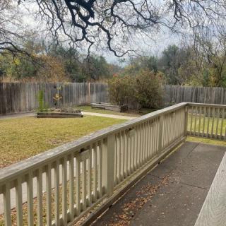 A backyard with a wooden deck, surrounded by a fence, featuring grass and garden beds.