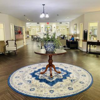 A welcoming lobby featuring a central round wooden table with a vase of flowers on an ornate circular rug.