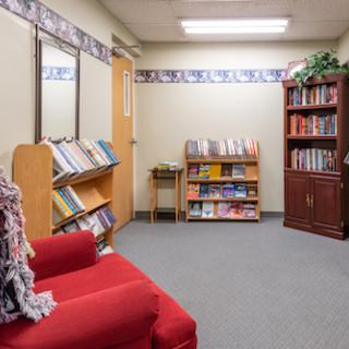 A cozy reading nook featuring shelves filled with books, a red sofa, and warm lighting.