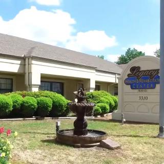 A building entrance with a decorative fountain and a sign on the lawn.