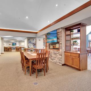 A spacious dining area with a large wooden table, surrounded by matching chairs, complemented by a carpeted floor and stylish shelving.