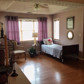 A cozy bedroom with a single bed, accented by purple curtains and a birdcage near the window.