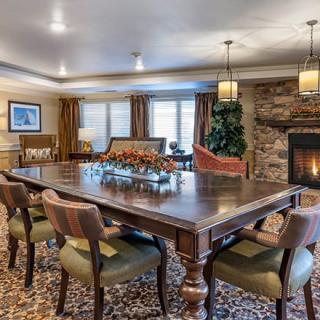 A cozy dining room featuring a large wooden table, surrounded by upholstered chairs, with a fireplace and elegant lighting.