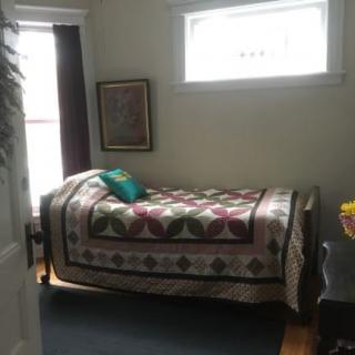 A cozy bedroom with a patterned quilt on the bed and artwork on the wall.