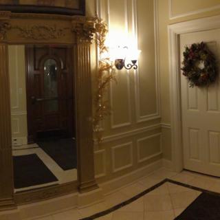 An elegant hallway featuring a large mirror, decorative lighting, and a door adorned with a wreath.