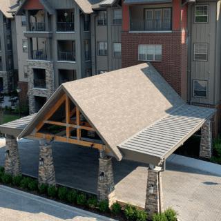 A modern apartment complex with a covered entrance featuring stone pillars and a pitched roof.