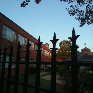 A view of a brick building behind an ornate fence under a clear sky.