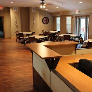 An empty restaurant dining area with neatly arranged tables and chairs, featuring a reception desk in the foreground.