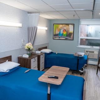 A well-designed patient room in a hospital, featuring two beds with blue bedding and modern furnishings.