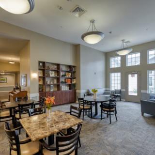 A well-lit dining area with multiple tables and chairs, featuring a bookshelf and decorative elements.