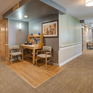 A cozy hallway nook featuring a wooden desk, two chairs, artwork on the wall, and soft lighting.