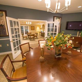 A well-lit dining room with a wooden table, chairs, and decorative elements, viewed through an open doorway.