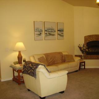 A cozy living room with a cream-colored sofa, a lamp on a side table, artwork on the wall, and a fireplace in the corner.