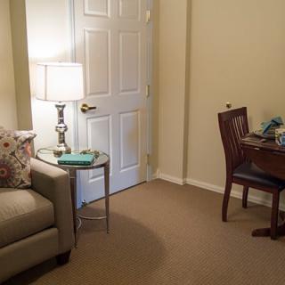 A cozy living room setup featuring a sofa, a lamp on a side table, and a small desk with a chair.