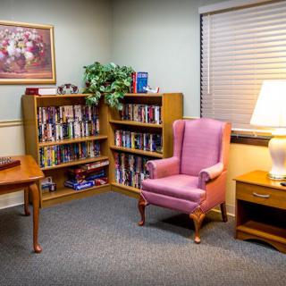 A cozy reading corner with a pink armchair, surrounded by bookshelves and a warm lamp.