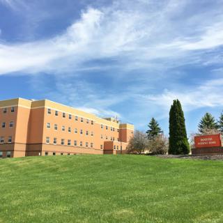 A sunny day showcasing a multi-story educational building surrounded by lush green grass and a clear blue sky.